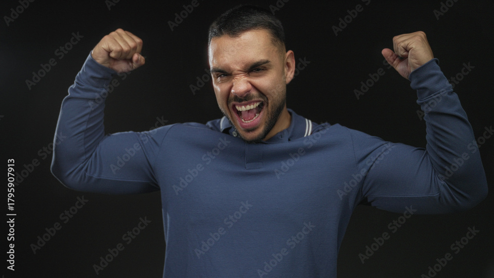 Naklejka premium Man flexes forearm and clenches fist to highlight muscle definition in black studio setting with dramatic lighting; triumph victory success winning.