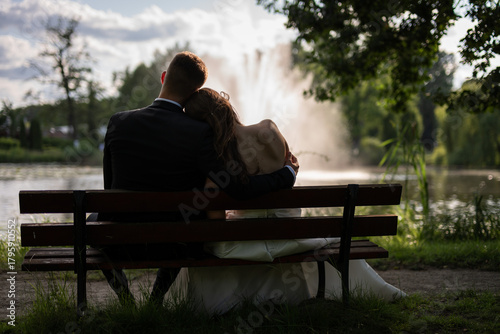 newly married couple hugging and sitting on a bench looking at the fountain