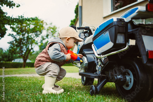 Little mechanic tinkers with toy motorcycle in sunny backyard on a cheerful afternoon