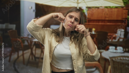 Photos Woman pulls cheeks downward and clenches fists in building while pouting expression; sadness frustration