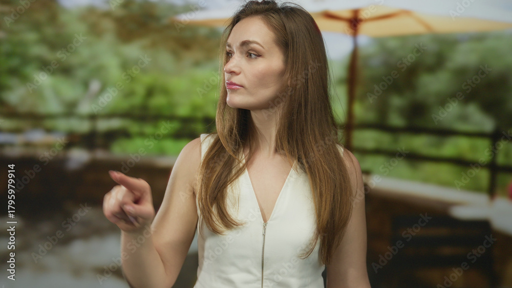 Obraz premium Young woman finger pointing to side on sunny building terrace overlooking green trees; determination.