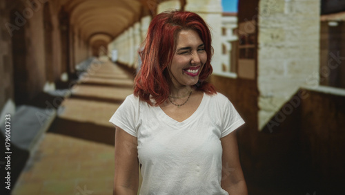 Free Download Woman smiling and winking in an old town street arcade with visible face, red hair and a white t shirt; carefree joy. - GFXLoad
