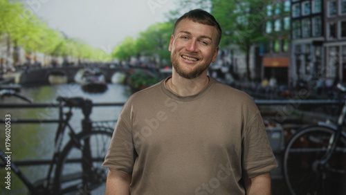 Photos Man with beard smiles on street in amsterdam canal area with bicycles and bridge; contentment leisure