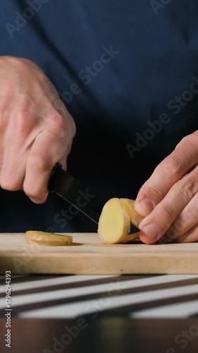 Vertical video. A man slices ginger root on a wooden cutting board, healthy preparation and natural detox lifestyle concept