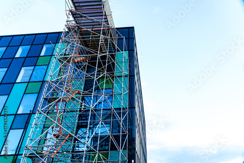 Green glass exterior of office building rising skyward with scaffolding