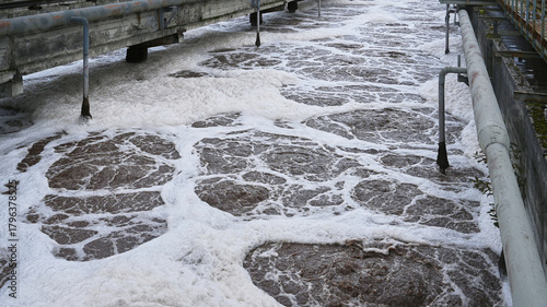 Treatment facility manages wastewater with foam on the surface during afternoon operations near urban area