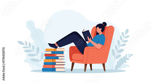 A person relaxing in an armchair reading a book with a stack of books next to them.