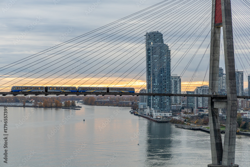 Naklejka premium Suspension Bridge Train Crossing Over Fraser River With Modern Vancouver Skyline At Sunset
