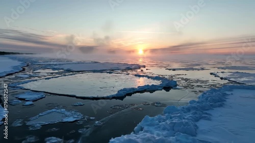 Icy expanse at dawn snowcovered ice floes scattered on dark water under a misty sky with a rising sun