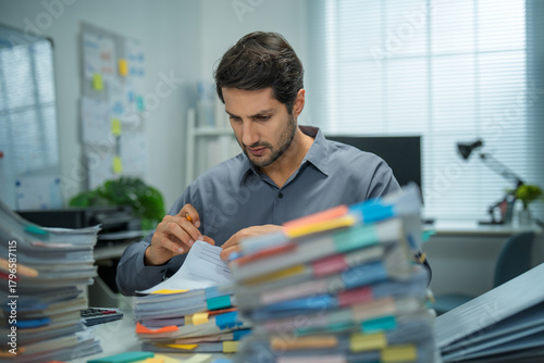 Hispanic businessman stressed over account mistakes, overwhelmed, tired, and facing deadlines in a busy office setting.
