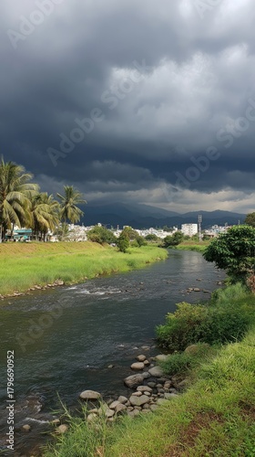 River under dark, stormy clouds. Green grass, trees, and distant mountains