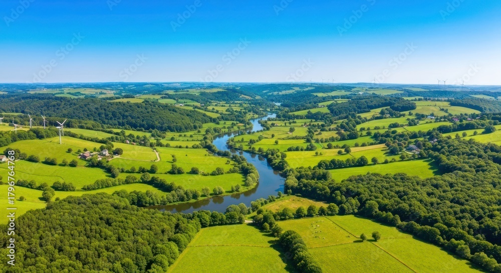 Obraz premium Panoramic view of lush green valley with river snaking through rolling hills under a blue sky