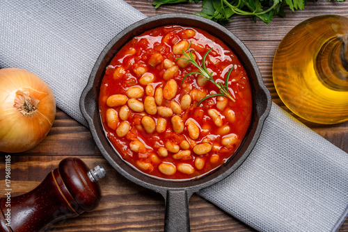 Baked bean dish in cast iron pan on wooden background.	