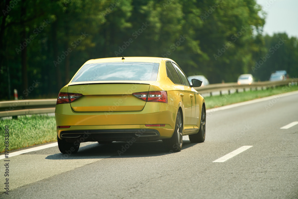 Fototapeta premium Yellow sedan driving on forest highway