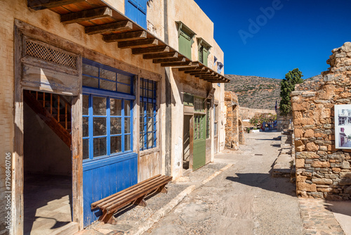 Historic courtyard on Spinalonga island with colorful wooden doors and stone architecture under bright summer sky