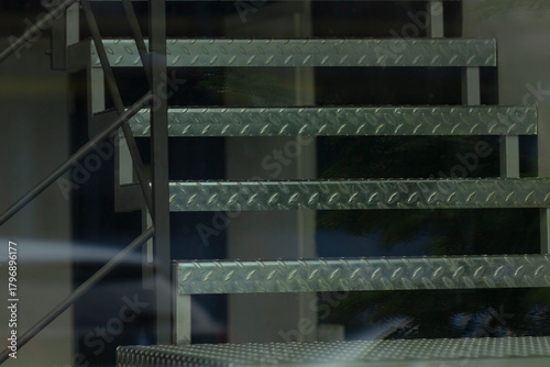 metal staircase reflected through glass facade, textured diamond plate treads and steel stringers visible
