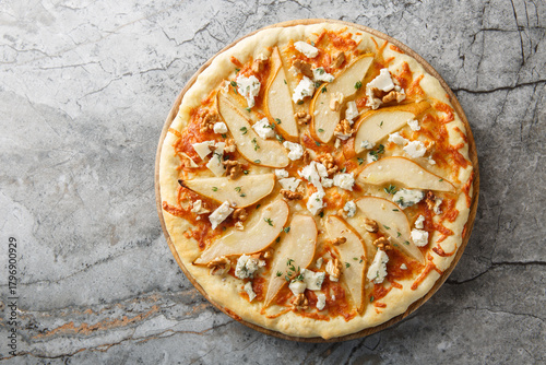 Sweet spicy pear pizza with blue cheese, walnuts, mozzarella and thyme close-up on a wooden board on the table. Horizontal top view from above