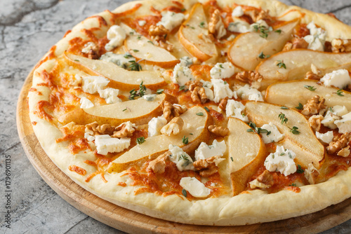 Honey pear pizza with blue cheese, nuts, mozzarella and thyme close-up on a wooden board on the table. Horizontal