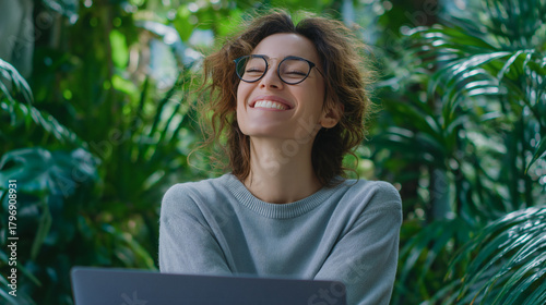 Fototapeta Naklejka Na Ścianę i Meble -  Joyful Woman with Glasses in Lush Greenhouse
