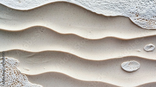 Fototapeta Naklejka Na Ścianę i Meble -  A detailed, abstract view of the ocean's edge, showing the interplay of light and shadow on wet, rippled sand and delicate sea foam.