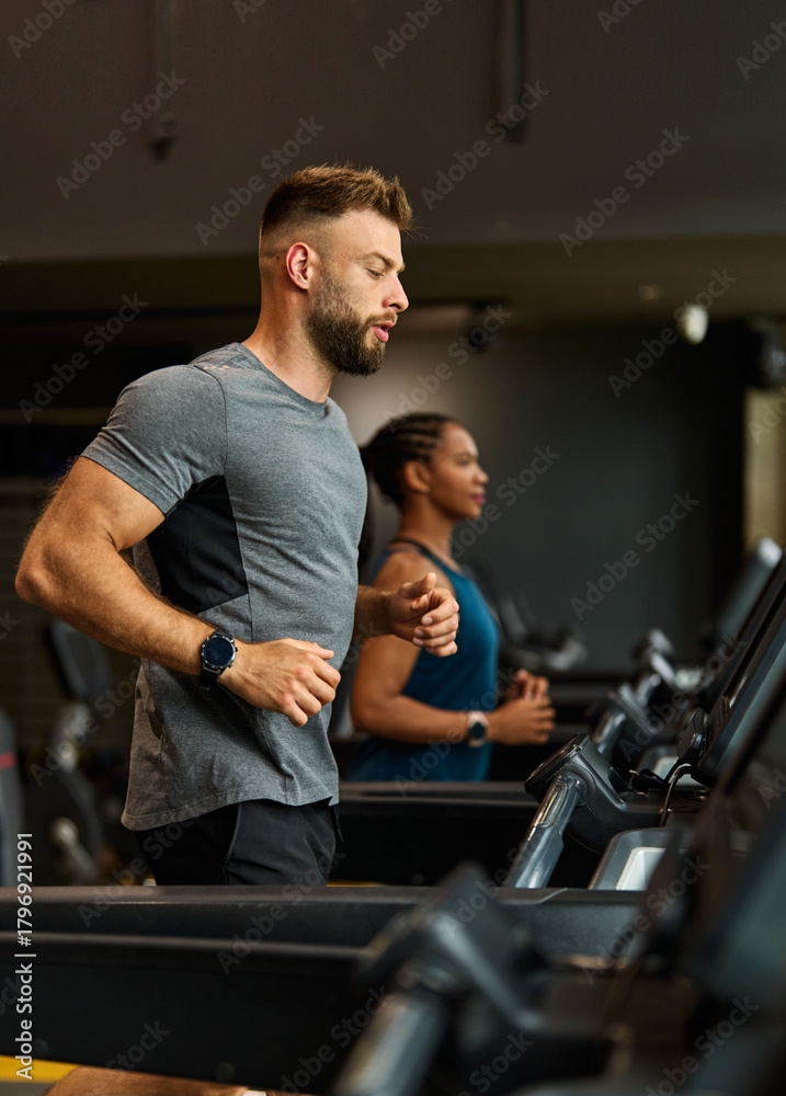 Fototapeta premium Portrait of a young man and a black woman exercising in a gym, running using thereadmill machine equipment, healthy lifestyle and cardio exercise at fitness club concepts