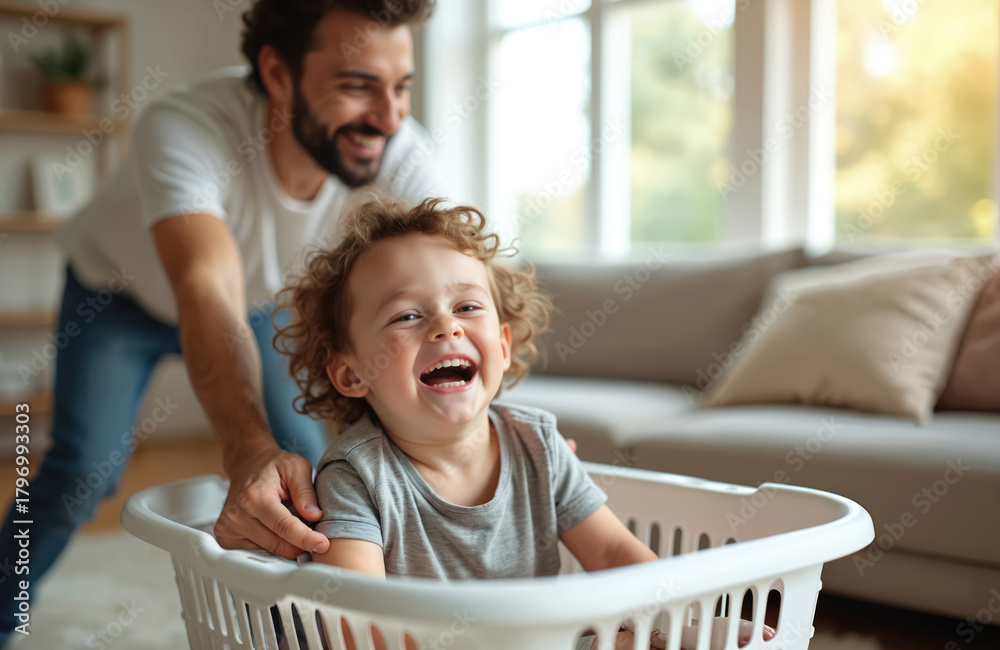 Obraz premium Father plays with son in laundry basket at home. Happy child laughs while dad pushes him around room. Family bonding, joyful moment, playful activity, domestic fun.