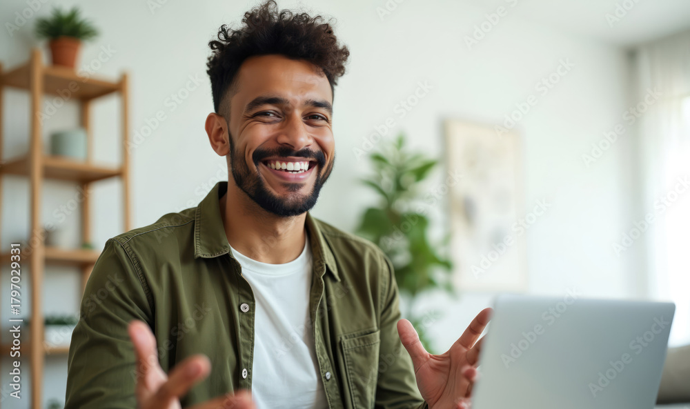 Naklejka premium Happy young man participates in video conference from home. He smiles at the camera talks and explains something. Male using laptop to communicate online. Remote work concept.