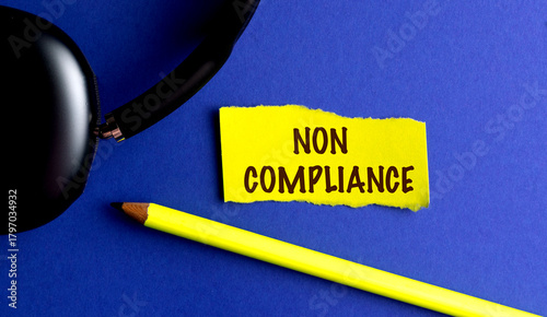 Non compliance message on torn yellow paper with pencil and black headset on blue background