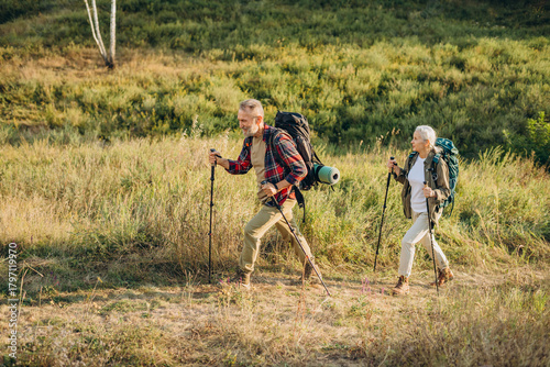 Active retired friends with canes travel exercising Nordic walking in park at sunset