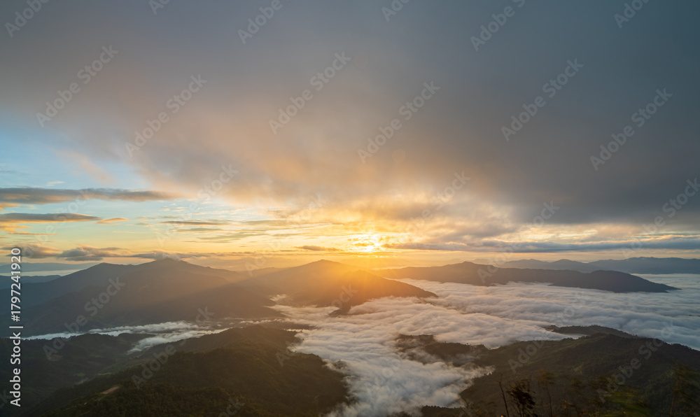 Fototapeta premium Sunlight breaking through clouds over mountain range and sea of mist, beautiful morning nature view.