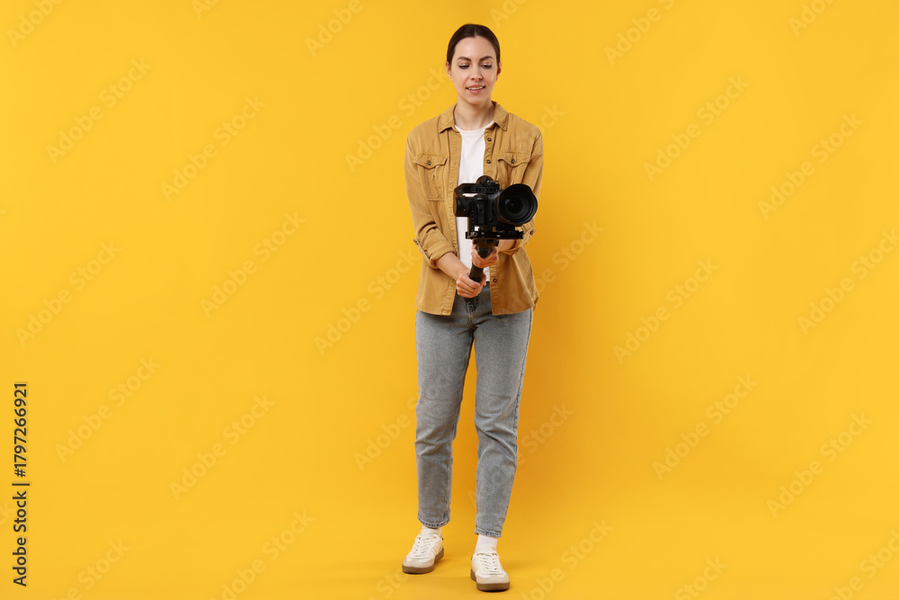 Fototapeta premium Videographer using gimbal stabilizer with camera on yellow background