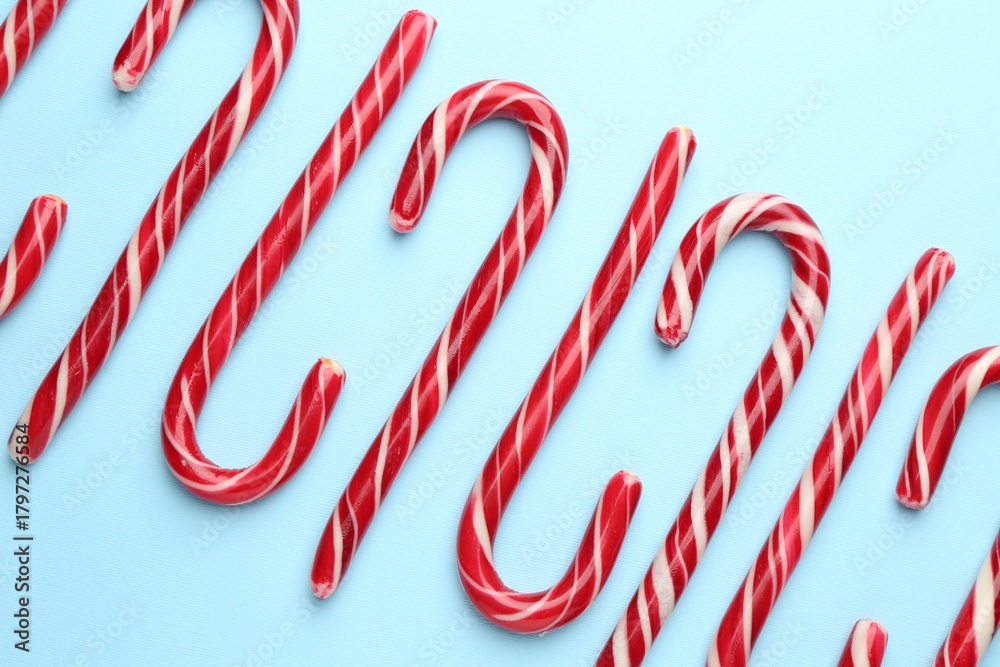 Obraz premium Tasty candy canes on light blue background, flat lay. Merry Christmas and Happy New Year