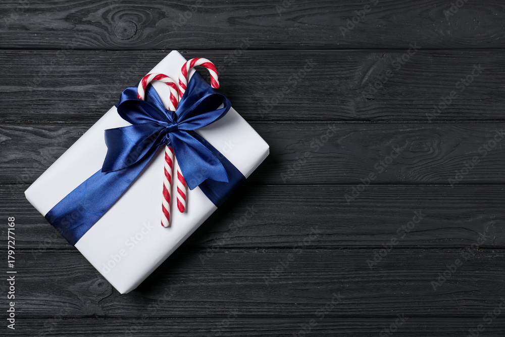 Obraz premium Decorated Christmas gift with candy canes on black wooden background, top view. Space for text