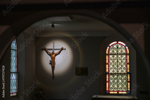 Inside Basilique Notre-Dame-de-Buglose, light casts a dramatic glow on a wooden crucifix and beautiful stained glass windows. This quiet moment captures the essence of peace and reflection.