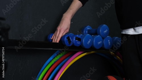 A man in the gym places dumbbells on a rack close-up of hands