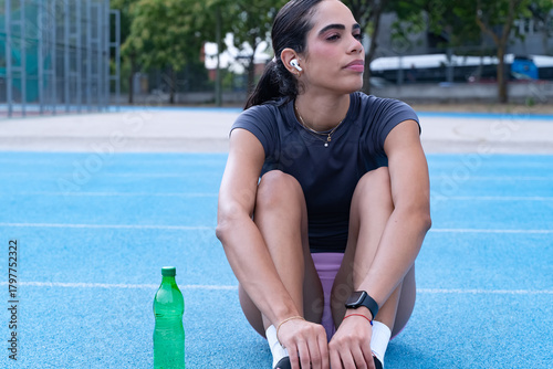 Young woman sitting on a blue sports track, recovering and reflecting after an exercise session