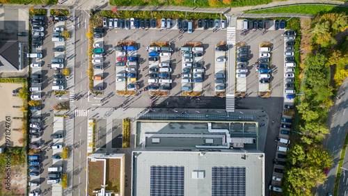 Aerial view of a busy parking lot filled with various vehicles, showcasing organized rows of cars and a modern building with solar panels on the roof