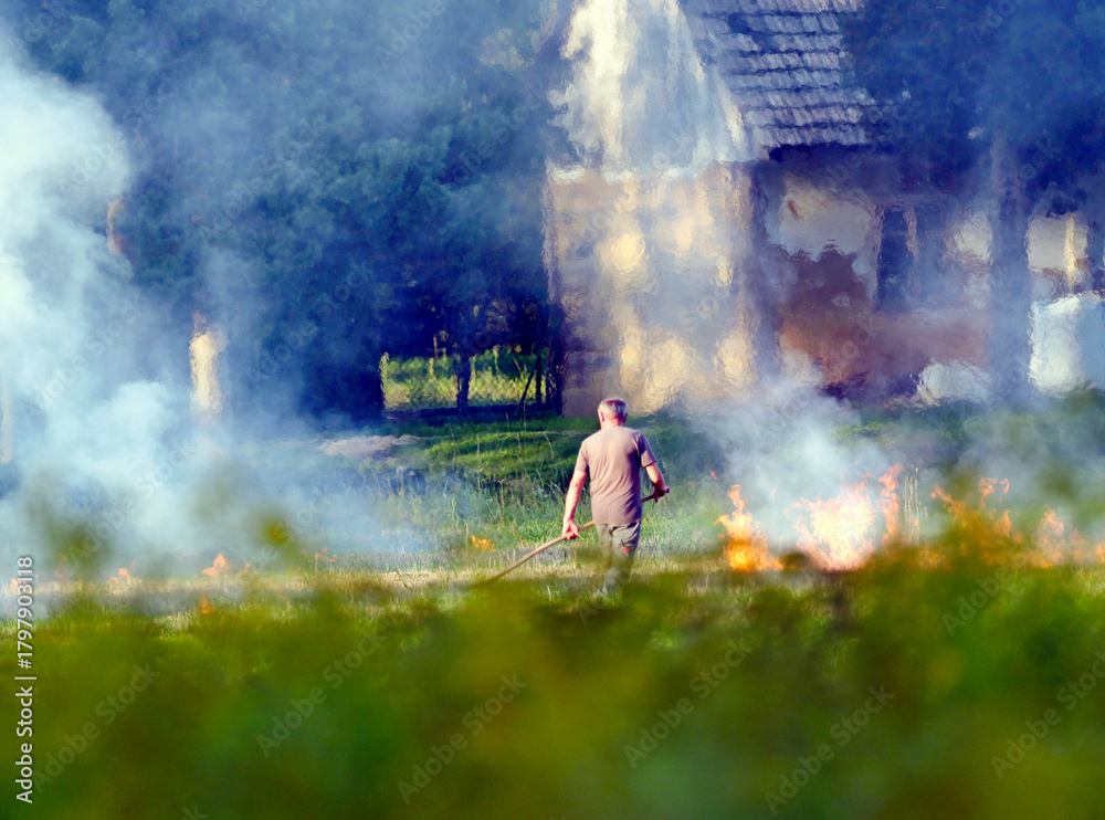 Fototapeta premium Mężczyzna wypala trawy na polu po zebraniu plonów. Wypalanie traw jest czynnością bardzo ryzykowną i szkodliwą dla środowiska