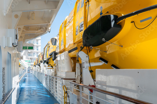 Billede på lærred Brightly colored yellow lifeboats line the deck of a large passenger ship under a clear blue sky