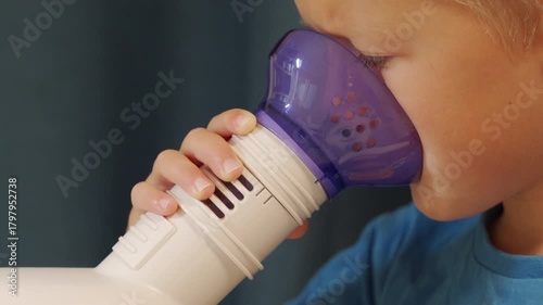 A young child holds a white and purple plastic nebulizer mask to their face, inhaling medicinal steam. This therapeutic action helps with breathing, creating a gentle and rhythmic breathing sound.