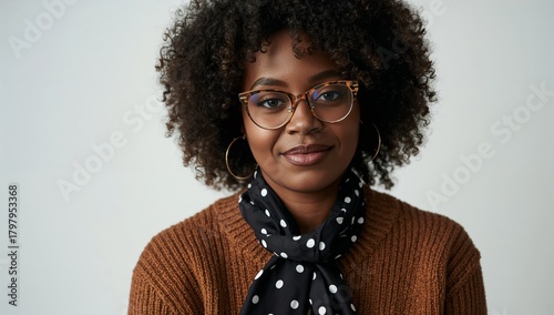 Young Woman With Curly Hair and Glasses Wearing a Scarf Poses Confidently Aga...