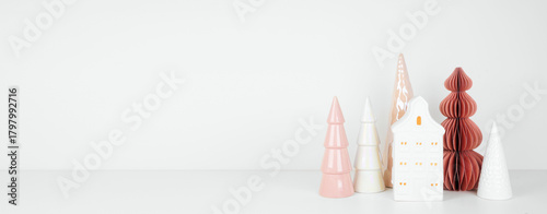 Pink and white Christmas house and tree decor on a white shelf against a white wall banner background with copy space
