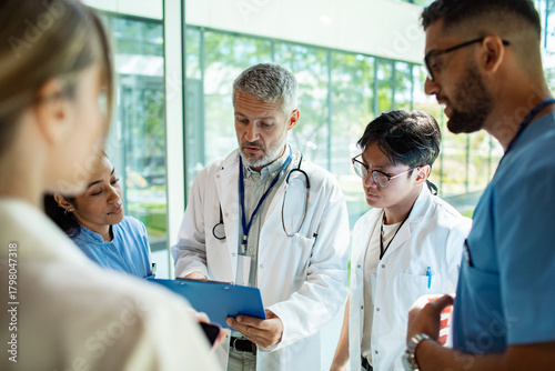 Mature doctor leading young adults in focused briefing at hospital