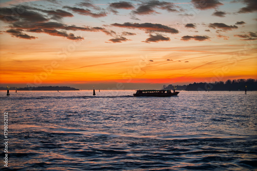 Backlight of a vaporetto at sunset. A vaporetto, in backlight, crosses the lagoon in a golden sunset on an autumn evening. Venice, Italy