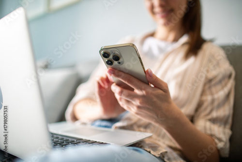 Young adult woman smiling using smartphone and laptop at home