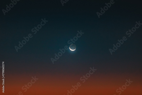 Sliver of moon over a sunrise gradient