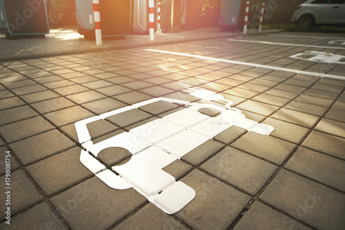 Close-up of electric vehicle parking symbol on paved charging area in warm evening light.