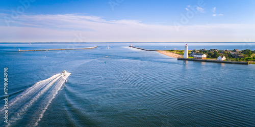 Heading to sea near Lynde Point Lighthouse and its adjacent keeper's house are viewed from an aerial perspective at sunset in Old Saybrook, Connecticut, New England.