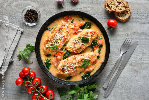 Chicken breast in creamy sauce with tomatoes and spinach on plate