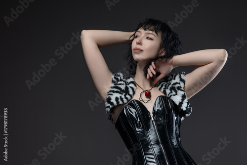 Gothic fashion: girl in glossy corset with checkered skirt, assertive pose on gray